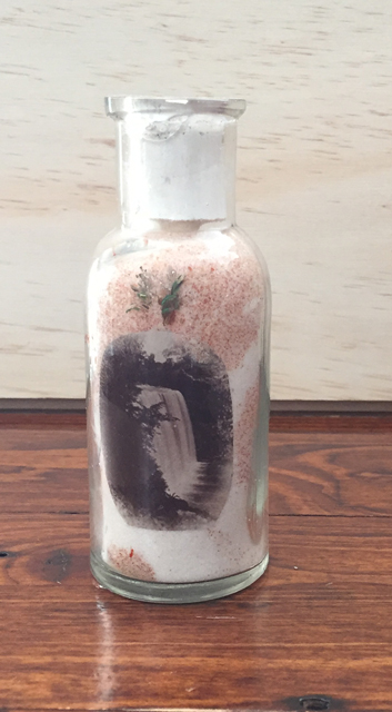 about 5 inches tall, a bottle of sand with a picture of the falls glued inside the clear glass.
