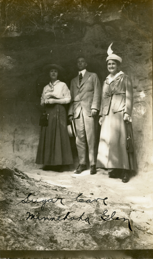 Three people from the late 19th or early 20th century, standing in a shallow cave.