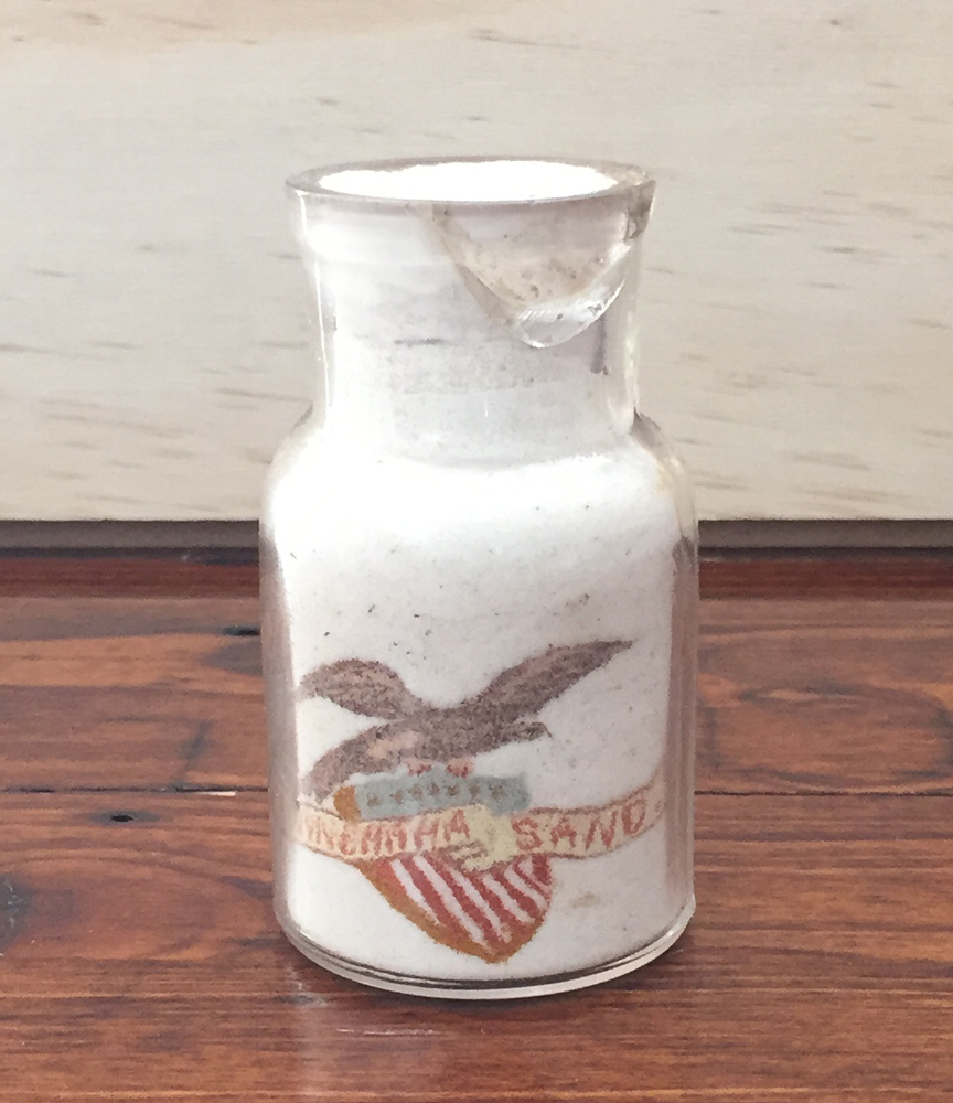 Shows an eagle standing on a shield showing stars and stripes, with a banner saying "Minnehaha Sand."