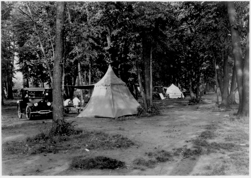 a couple of tents, and some cars among the trees in a campground