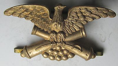 an eagle, wings spread, facing right, clutching 2 crossed cannons in its talons.