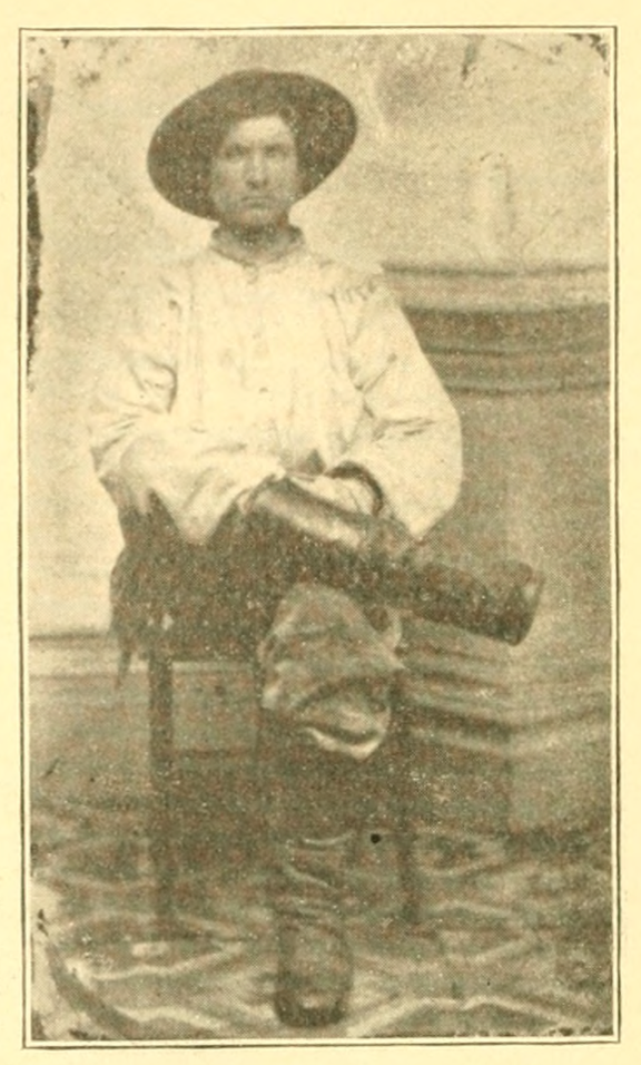 A young man sits for a studio portrait. He is wearing some very prominent boots.