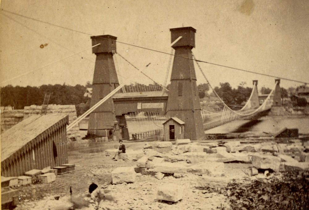 A few of a wooden bridge, with 2 towers on each side of the bridge. The area around the bridge is messy.